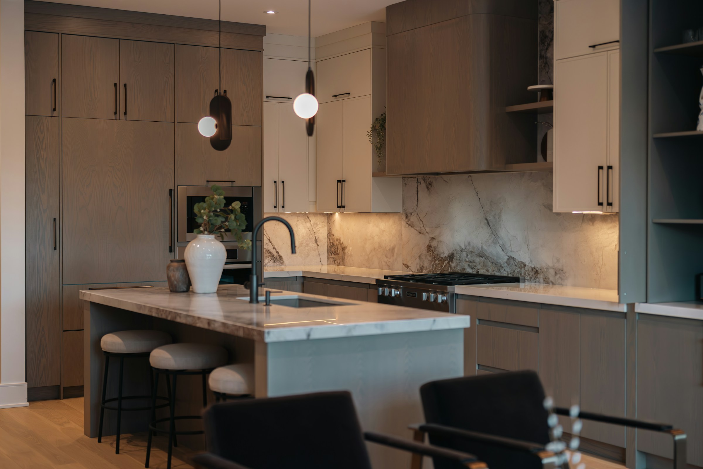 Contemporary kitchen with warm wood cabinetry, sculptural lighting, and veined stone surfaces